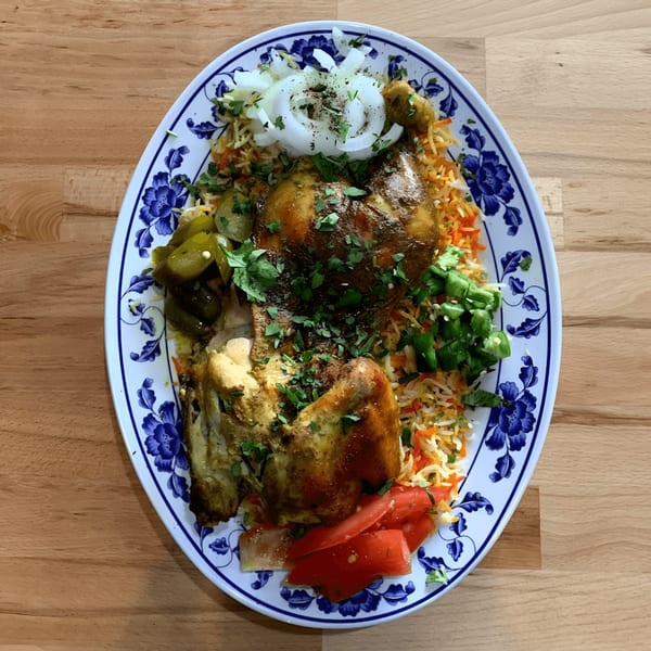 A large platter of Ali Baba Kabab's Mediterranean chicken and rice, garnished with vegetables.
