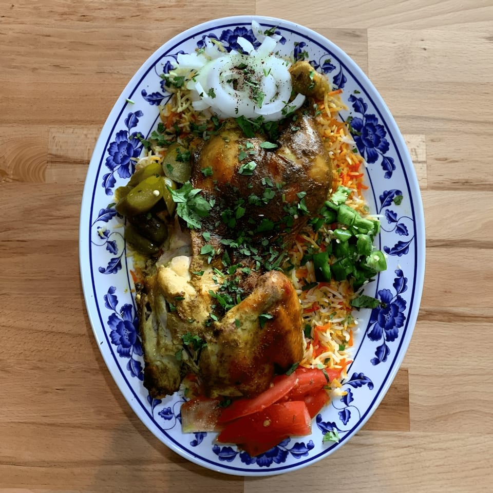 A large platter of Ali Baba Kabab's Mediterranean chicken and rice, garnished with vegetables.