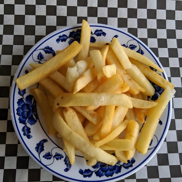 A white plate with blue floral designs filled with golden french fries on a checkered tablecloth.
