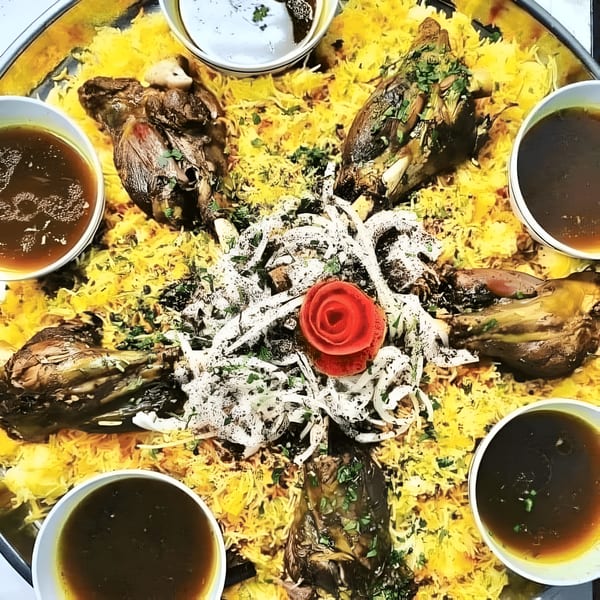 A large platter of Mediterranean rice with roasted lamb shanks, garnished with onions and a red rose.