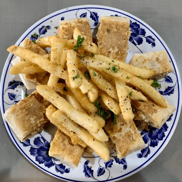 Mediterranean shawarma wraps and seasoned french fries on a white plate with blue floral patterns.