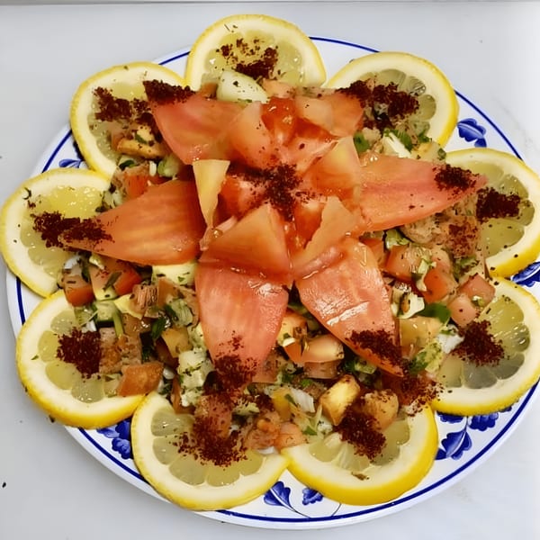 Mediterranean salad with chopped vegetables, tomatoes, and lemon slices, garnished with sumac.