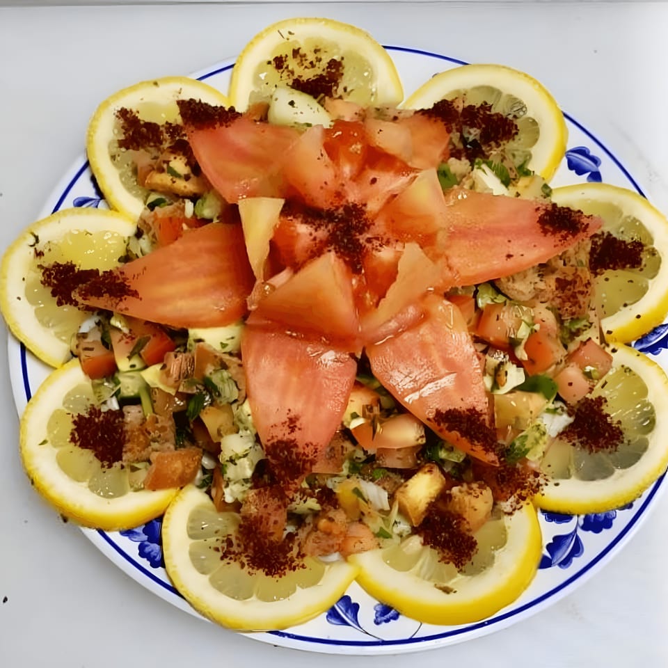 Mediterranean salad with chopped vegetables, tomatoes, and lemon slices, garnished with sumac.