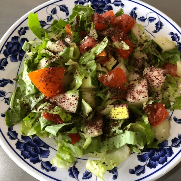 A fresh Mediterranean salad with lettuce, tomatoes, cucumbers, and sumac on a blue and white plate.